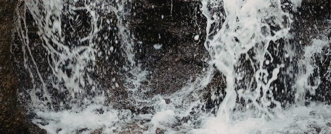 Water splashing over rocks, creating white foam and spray in a close-up scene.