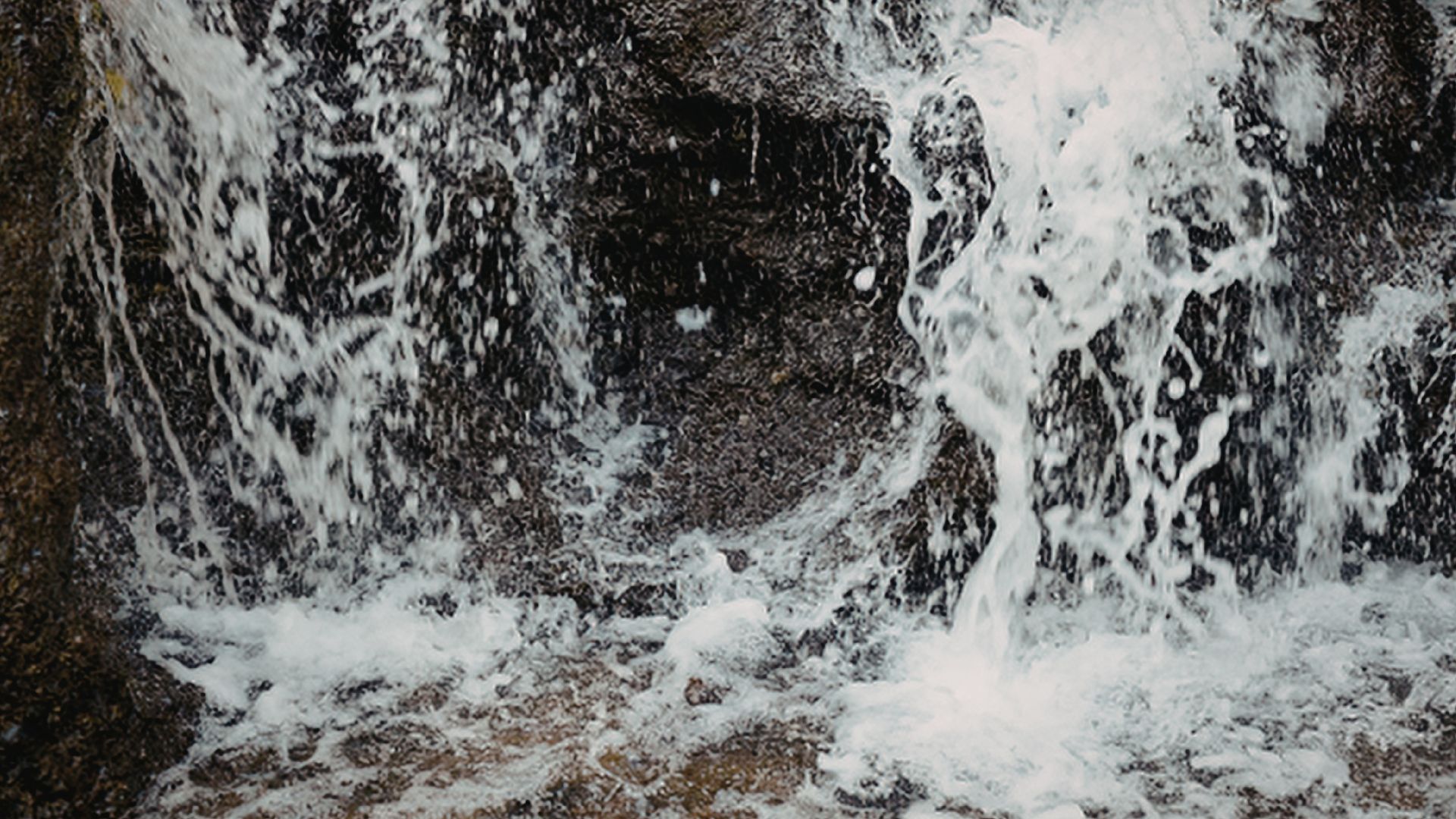 Water splashing over rocks, creating white foam and spray in a close-up scene.